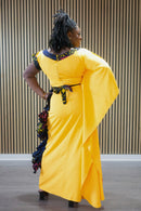 Person wearing a bright yellow dress with decorative elements, standing against a wooden panel background.