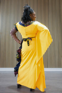 Person wearing a bright yellow dress with decorative elements, standing against a wooden panel background.