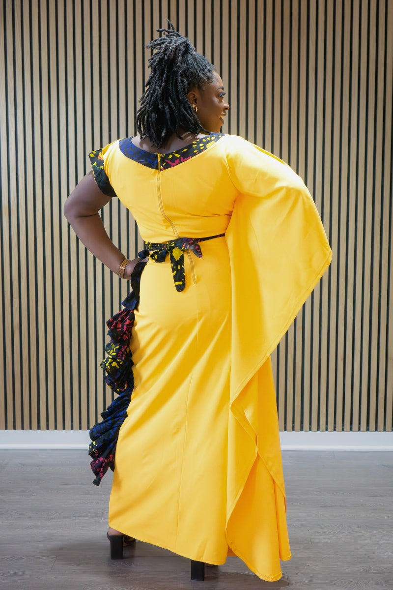 Person wearing a bright yellow dress with decorative elements, standing against a wooden panel background.